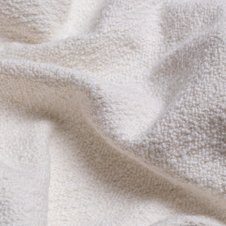 A close-up of a soft, textured off-white fabric with a plush, bouclé-like surface, shown in gentle folds.