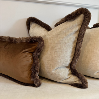 Three decorative pillows with brown trim on a beige sofa.