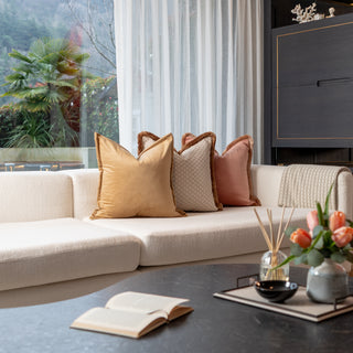 Modern living room with a beige sectional sofa, decorative pillows, and a coffee table with a book and flowers.