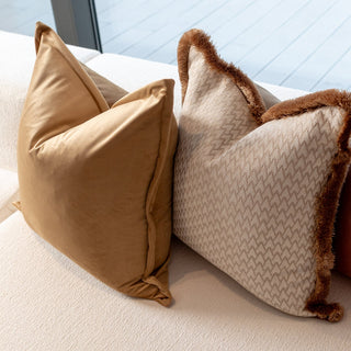 Three decorative pillows in brown, beige, and terracotta colors on a light-colored sofa.