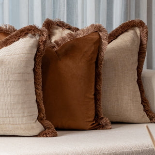 Four decorative pillows with brown trim on a beige sofa.
