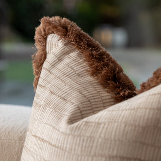 Close-up of a textured beige pillow with brown trim on a blurred outdoor background